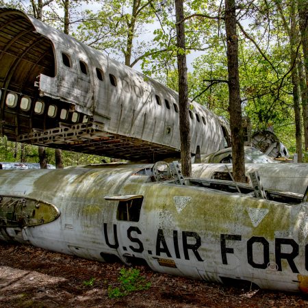 Salvage yard with abandoned U.S. Air Force fighter jet and airplane fuselage in treed setting .