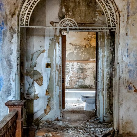 Abandoned Manor House with arch doorway, peeling paint and carved molding.