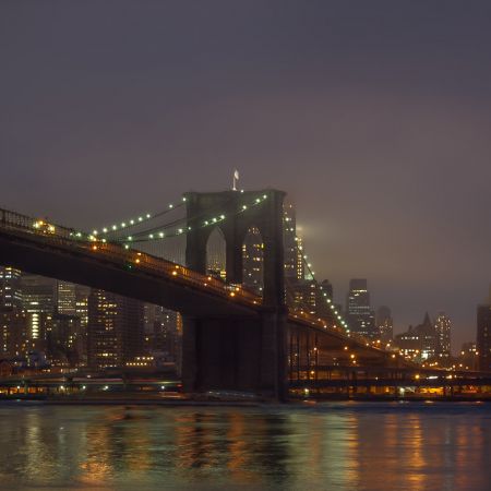 DUMBO on a foggy night featuring Brooklyn Bridge and cityscape.