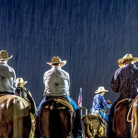 Cowboys and cowgirls on horses in rain downpour at rodeo in Maryland.