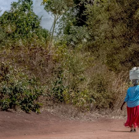 Kenyan woman balancing large bag on her head as she walks down a road.