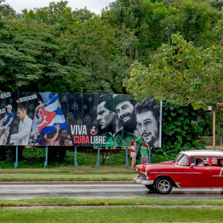 Classic Cuban car driving past Revolutionary Square and a billboard noting Long Live Free Cuba and Che Guevara.