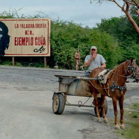 Cuban country road outside Havana with billboard of Che Guevara and man with horse and buggy.