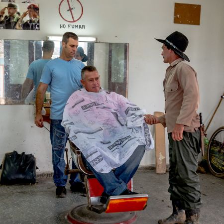 Barbershop in Vinales with man getting hair cut and one wearing cowboy hat and knife attached to belt.