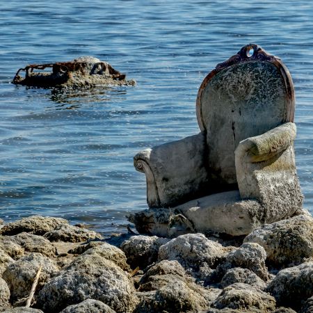 Abandoned upholstered chair beach and at water's edge in Salton Sea, California.