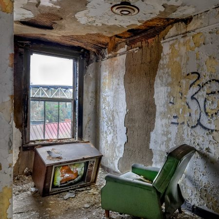 Abandoned boarding room with broken television, recliner and peeling paint.