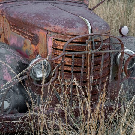 Rusted 1930s farm truck with metal grill and headlight protector.