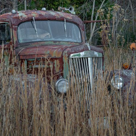 Rusted White Superpower 1930s truck in field of tall grass.