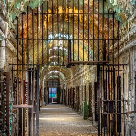 Abandoned cell block in prison with sheets of peeling paint, skylights and iron bars.