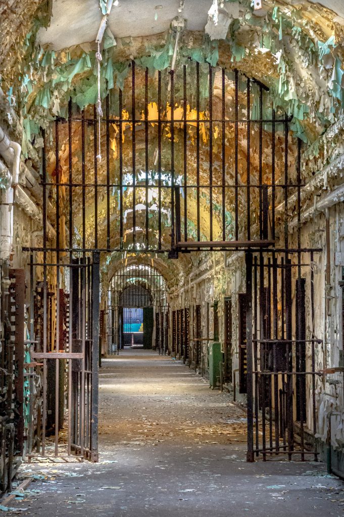 Abandoned cell block in prison with sheets of peeling paint, skylights and iron bars.