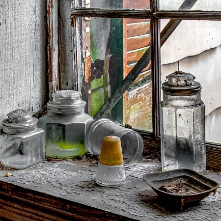 A still life of forgotten kitchen glassware resting on a sill of peeling paint.