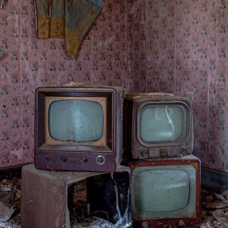 Abandoned rural farm house with peeling wallpaper, crumbling flooring and a stack of vintage black and white televisions.