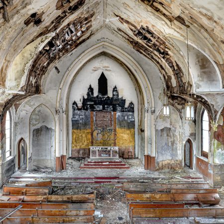 Abandoned church with cathedral ceiling, chandeliers, wood pews, alter, arched doorways and windows, and graffiti.