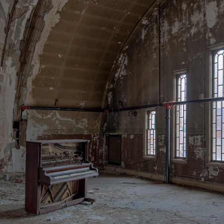 Ballroom of abandoned shriners temple with peeling paint, tall windows, piano and high ceilings.