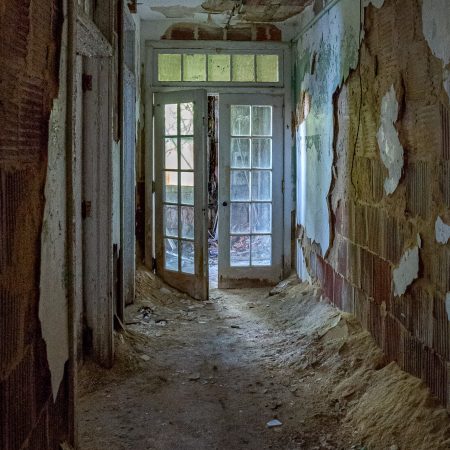 Abandoned Hospital doorway to veranda and peaks and valleys of deteriorating walls.