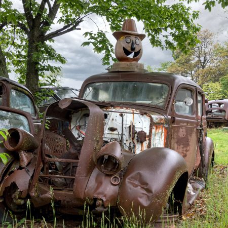 Rusty 1930s car shell with jack-o-lantern artifact on vehicle roof.