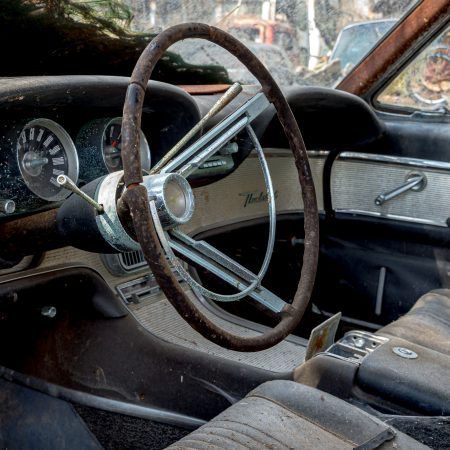 Interior of 1960s Ford Thunderbird with cobwebs and slotted brake and gas pedals.