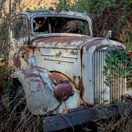 Vintage rusty and white enameled Mack truck with bulldog grill ornament.