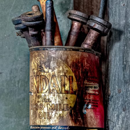 Vintage textile factory wooden bobbins in a 1940s oil can with classic car, truck and boat illustrations the bottom band of can.