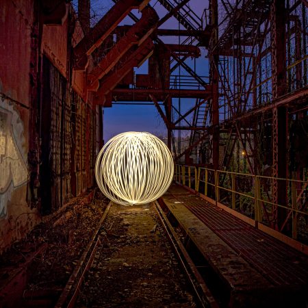 Light string spinning at blue hour on US Steel's Carrie Blast Furnace rusted train trestle elevated platform.