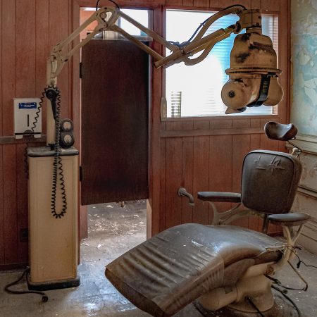 A shuttered dental office with dental chair and x-ray machine amid the peeling paint and crumbling walls.