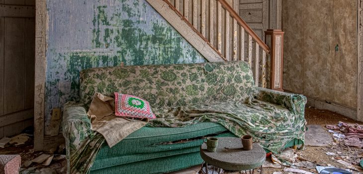 Abandoned house living room with sofa, peeling paint, crocheted pillow and upholstered couch.