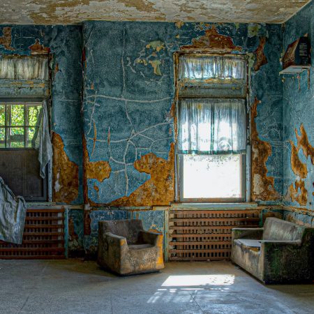 The common area lounge of an abandoned asylum holding peeling paint and moldy furniture.