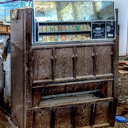 A vintage cigarette vending machine is discarded in an abandoned beachside club.