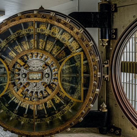 A brass and glass bank vault door with elaborate ornamentation and etching.