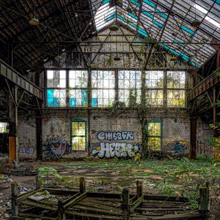 Abandoned Machine Factory with skylight ceiling, green vines, interior trees and graffiti.