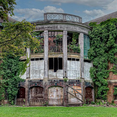 Vines and boards cover the windows of a curved wing of an abandoned public hospital.