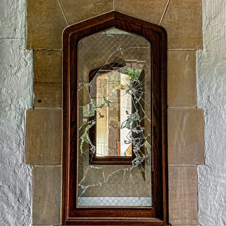 The broken wired window framed by stone and stucco in a derelict prison building lobby.