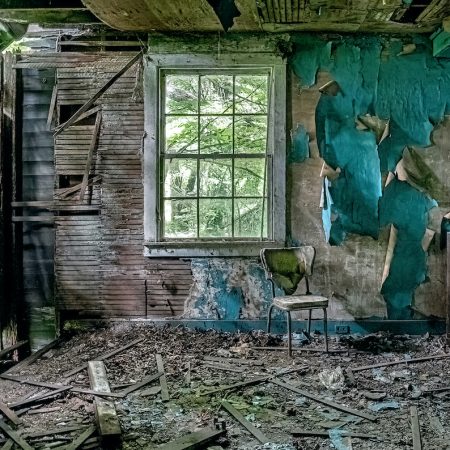 A 1950s era television sits in a crumbling room with peeling paint, holes in the floor and a curved back kitchen chair.